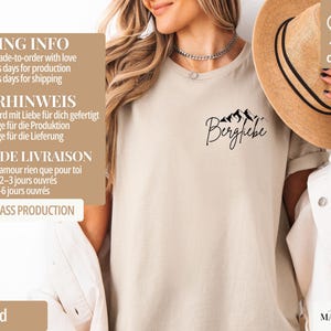 May include: Sand-colored t-shirt with the word "Bergfiebe" and a mountain graphic in black. The shirt is made of 100% cotton. A straw hat is visible in the background. The shirt is from the brand "simply MARGUERITE".