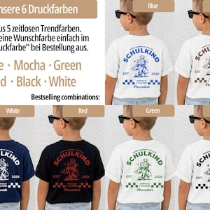 May include: A collection of short-sleeved t-shirts featuring a back graphic with the text SCHULKIND, EST 2026, and a cartoon character. The shirts are shown in white, navy, and black with print colors including blue, mocha, green, red, black, and white.