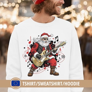 Könnte beinhalten: Weißes Sweatshirt mit einer Grafik von Santa Claus, der E-Gitarre spielt. Santa trägt eine Sonnenbrille, einen roten Anzug und eine schwarze Lederweste. Noten und Schneeflocken umgeben Santa. Der Text "TSHIRT/SWEATSHIRT/HOODIE" befindet sich unten.