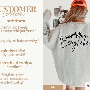 May include: Light grey sweatshirt with a black mountain graphic and the word "Bergfliebe". The sweatshirt is ash-colored and has customer reviews on the left side. The brand name "simply MARGUERITE" is at the bottom right.