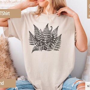Puede incluir: Camiseta color arena con un dise&ntilde;o de helecho negro. La camiseta tiene mangas cortas y cuello redondo. El texto "TShirt" est&aacute; en un rect&aacute;ngulo marr&oacute;n en la parte superior izquierda. Hecha de 100% algod&oacute;n.