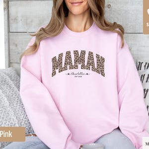 Op de afbeelding: Lichtroze sweatshirt met het woord "MAMAN" in een luipaardprint. Daaronder staan de naam "charlotte" en de tekst "est 2020". De trui heeft een ronde hals en lange mouwen.