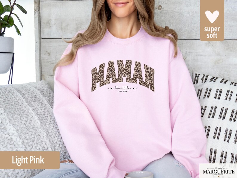 Op de afbeelding: Lichtroze sweatshirt met het woord "MAMAN" in een luipaardprint. Daaronder staan de naam "charlotte" en de tekst "est 2020". De trui heeft een ronde hals en lange mouwen.