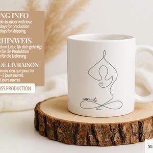 May include: White ceramic mug with a black line drawing of a person in a yoga pose, with the word "namaste" below. The mug is on a wooden slice. The mug has a curved handle.