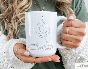 May include: White ceramic mug featuring a black line drawing of a yoga pose with a heart. The mug has the word "namaste" and the name "Sophie" in a script font. The mug is held by a person.