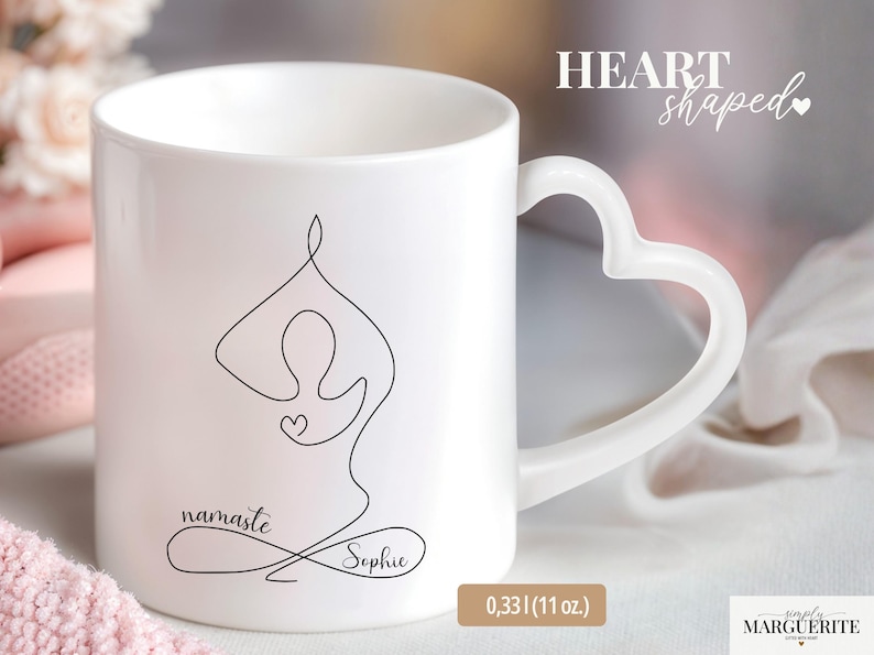 May include: White ceramic mug with a heart-shaped handle. The mug features a black line drawing of a yoga pose, the word "namaste", and the name "Sophie". The mug holds 11 oz.