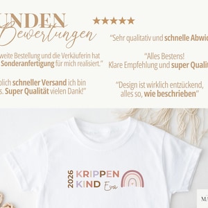 May include: A white t-shirt featuring the text 2026 KRIPPEN KIND Eva and a small rainbow graphic. The image includes German customer reviews with five stars, stating: Kunden Bewertungen, Sehr qualitativ und schnelle Abwicklung, Meine zweite Bestellung, Alles Bestens, Klare Empfehlung, Unglaublich schneller Versand, Super Qualit&auml;t, Design ist wirklich entz&uuml;ckend, alles so wie beschrieben.