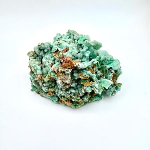 May include: A close-up of a mineral specimen with a textured surface. The mineral has a light green color with areas of brown and gold. The specimen is set against a white background.