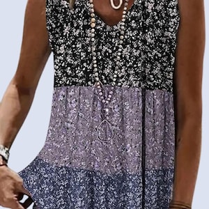 May include: Sleeveless floral print top in black, lavender, and navy blue. The top features a V-neck and a layered design with a floral pattern. A long beaded necklace with a teardrop pendant is visible.