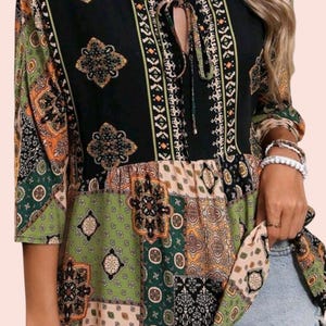 May include: A black, green, and orange patterned top with a V-neckline and tie detail. The top features a patchwork design with floral and geometric motifs. The sleeves are three-quarter length.