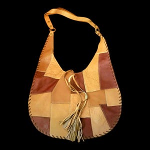 May include: A hobo-style shoulder bag constructed from various rectangular patches of tan, light brown, and dark brown leather. The bag features a single shoulder strap, visible whipstitch detailing along the edges, and a leather tassel accent.