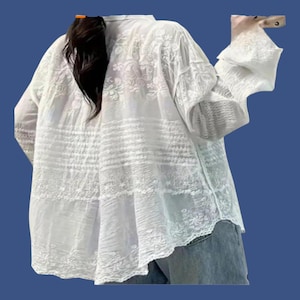 May include: White, long-sleeved blouse with floral embroidery and a loose fit. The blouse features a button-down front and a delicate, semi-sheer fabric. The sleeves are three-quarter length, and the hemline is slightly curved.