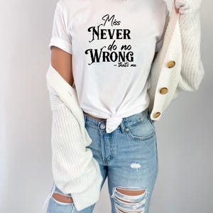 May include: White t-shirt with the text "Miss Never do no Wrong - that's me" in black script. The shirt is paired with light blue ripped jeans and a white cardigan.