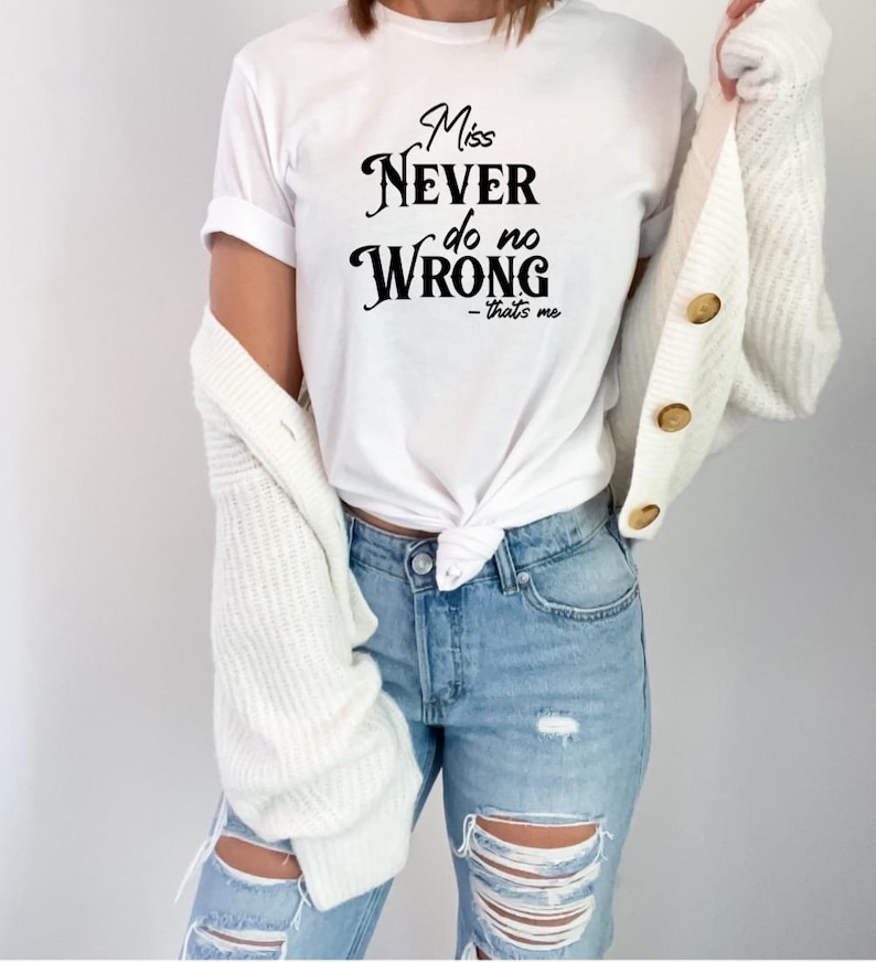 May include: White t-shirt with the text "Miss Never do no Wrong - that's me" in black script. The shirt is paired with light blue ripped jeans and a white cardigan.