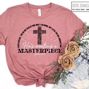 May include: A dusty rose t-shirt with the text "He's creating a MASTERPIECE" and the Bible verse John 13:7. The design includes a cross made of words like "trials" and "grief". The shirt is styled with denim shorts and floral accents.