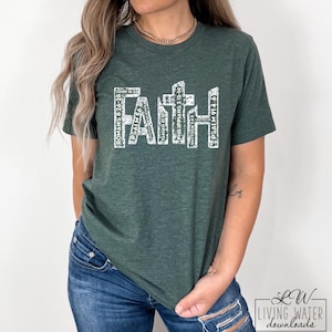 May include: Dark green t-shirt featuring the word "FAITH" in white block letters. The word "FAITH" is composed of various Bible verses. The shirt has a crew neck and short sleeves. The t-shirt is made of a soft material.