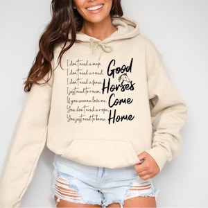 May include: Cream-colored hoodie with a front pocket and drawstring. The hoodie features black text that reads "Good Horses Come Home" with additional text above and below the main phrase. The design includes a horse graphic.