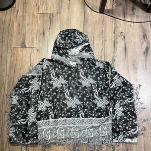 May include: A black and white paisley hooded scarf with fringe. The scarf features a repeating paisley pattern in white against a black background. The bottom edge has a decorative border and fringe.