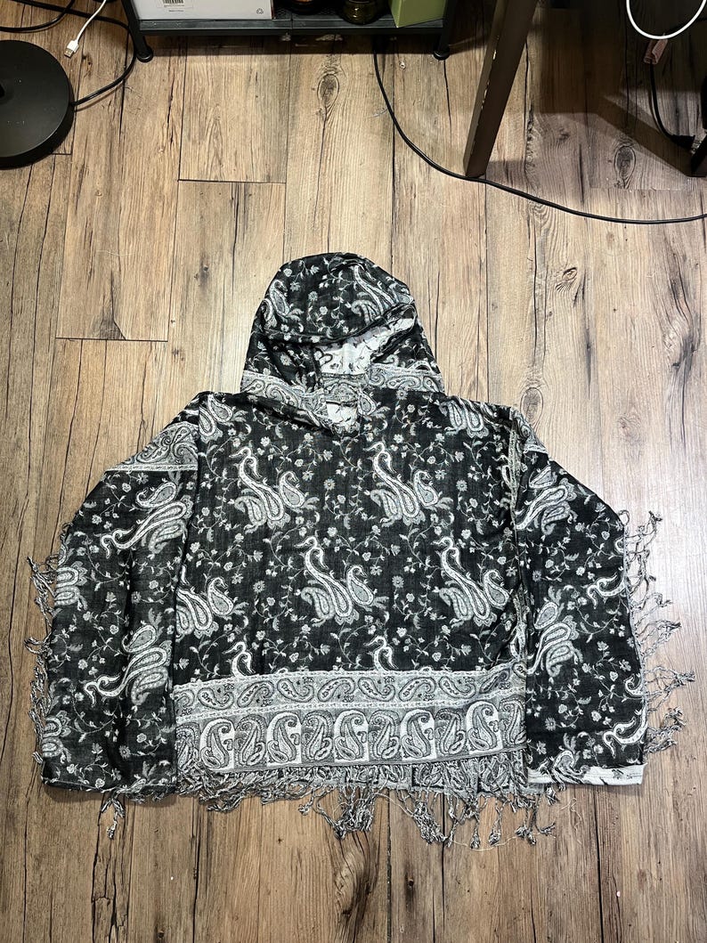 May include: A black and white paisley hooded scarf with fringe. The scarf features a repeating paisley pattern in white against a black background. The bottom edge has a decorative border and fringe.