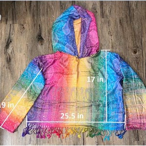 May include: A rainbow-colored hooded poncho with a paisley pattern. The poncho measures 25.5 inches wide, 17 inches long, and the sleeves are 19 inches long. The bottom edge has a fringe of colorful tassels.