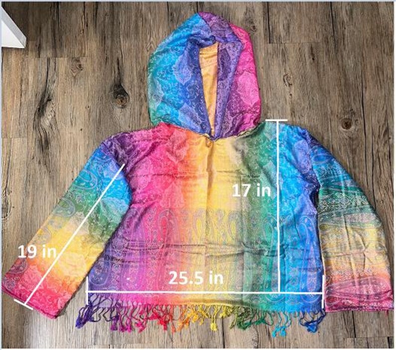 May include: A rainbow-colored hooded poncho with a paisley pattern. The poncho measures 25.5 inches wide, 17 inches long, and the sleeves are 19 inches long. The bottom edge has a fringe of colorful tassels.