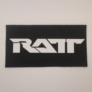 May include: A black rectangular patch with the white word "RATT" in a bold, stylized font. The patch has a textured surface and is likely made of fabric.