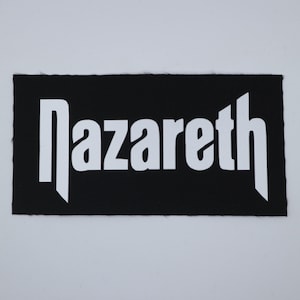 May include: A black rectangular patch with the word "Nazareth" in white, stylized lettering. The patch has a textured surface and is likely made of fabric. The design is simple and bold, with a clear contrast between the black background and white text.