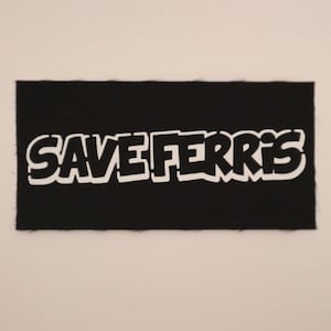 May include: A black rectangular patch with the words "SAVE FERRIS" in bold, white, block letters. The patch has a textured surface and a white border around the letters. The patch is centered on a light beige background.