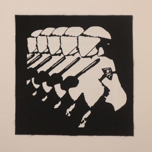 May include: Black and white patch featuring a marching line of soldiers in helmets, carrying rifles. The soldiers are depicted in a stylized, silhouette-like design. A small emblem is visible on one soldier's arm.