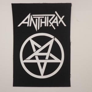 May include: Black and white patch with the band name "Anthrax" in a bold, stylized font and a white pentagram with a stylized "A" inside.