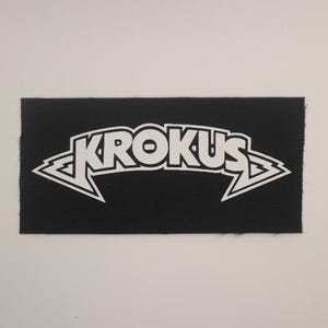 May include: Black fabric patch with a white "KROKUS" logo in a stylized font with lightning bolt accents.