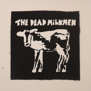 May include: Black square patch with the text "THE DEAD MILKMEN" in white block letters above a white cow illustration. The cow is stylized with black and white markings.