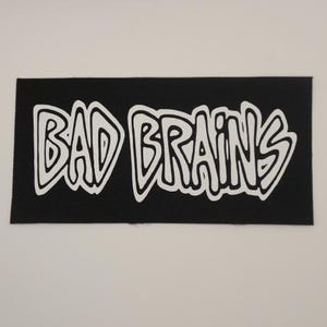 May include: Black patch with white lettering that reads "BAD BRAINS" in a stylized font.