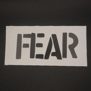 May include: White fabric patch with the word "FEAR" printed in black.