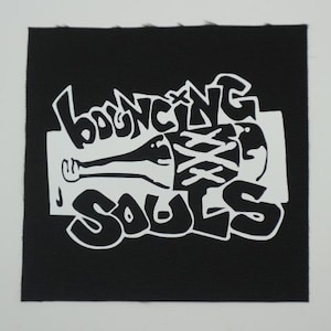 May include: Black square patch with the words "Bouncing Souls" in white, stylized graffiti font. A white graphic of a figure with an arm and a wrapped torso is in the center. The patch has a textured appearance.