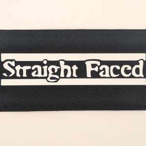 May include: A black rectangular patch with the words "Straight Faced" in white, stylized font. The text is centered within a white horizontal bar. The patch has a textured appearance.