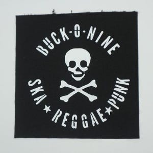 May include: Black square patch with white text and a skull and crossbones design. The text reads "BUCK-O-NINE" at the top, "SKA" and "PUNK" on the sides, and "REGGAE" at the bottom.