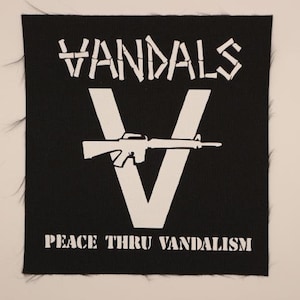 May include: Black square patch with white text and graphics. The word "VANDALS" is at the top. A large white "V" is in the center, with a rifle superimposed on it. The text "PEACE THRU VANDALISM" is at the bottom.
