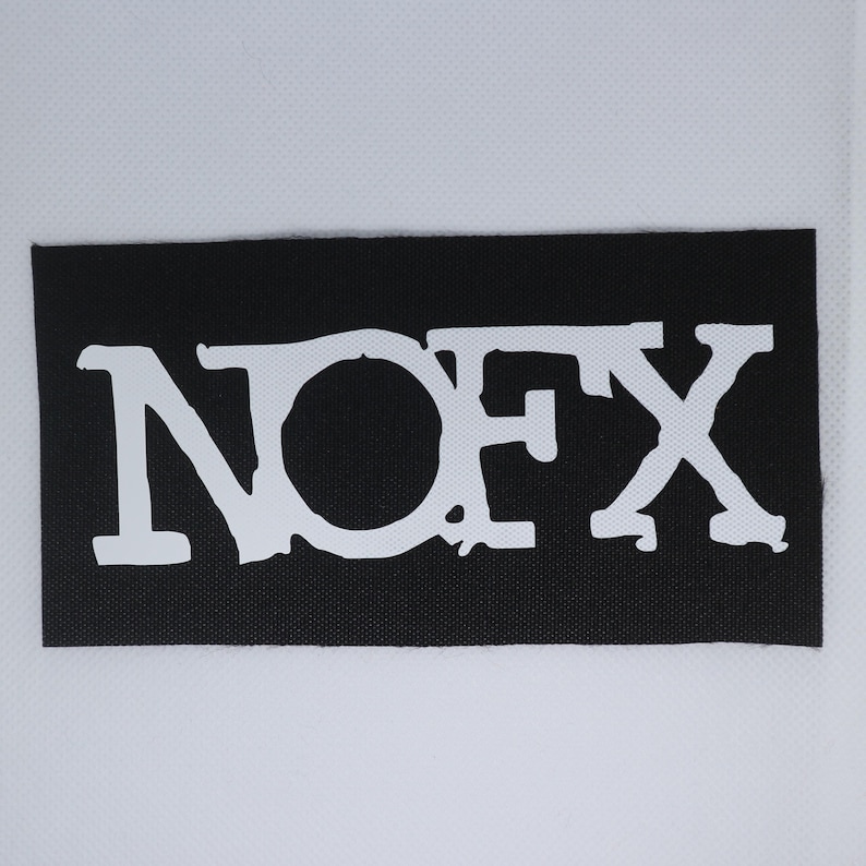 Peut inclure: Un patch rectangulaire noir avec le texte blanc "NOFX". Les lettres sont stylis&eacute;es et l&eacute;g&egrave;rement us&eacute;es, avec un aspect textur&eacute;. Le patch est probablement destin&eacute; aux v&ecirc;tements ou accessoires.