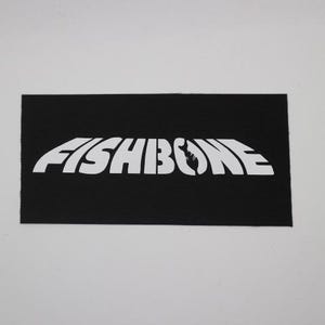 May include: A black rectangular patch with the white text "FISHBONE". The word "FISHBONE" is in a stylized font, with a fish skeleton graphic replacing the letter "O". The patch has a ribbed texture.
