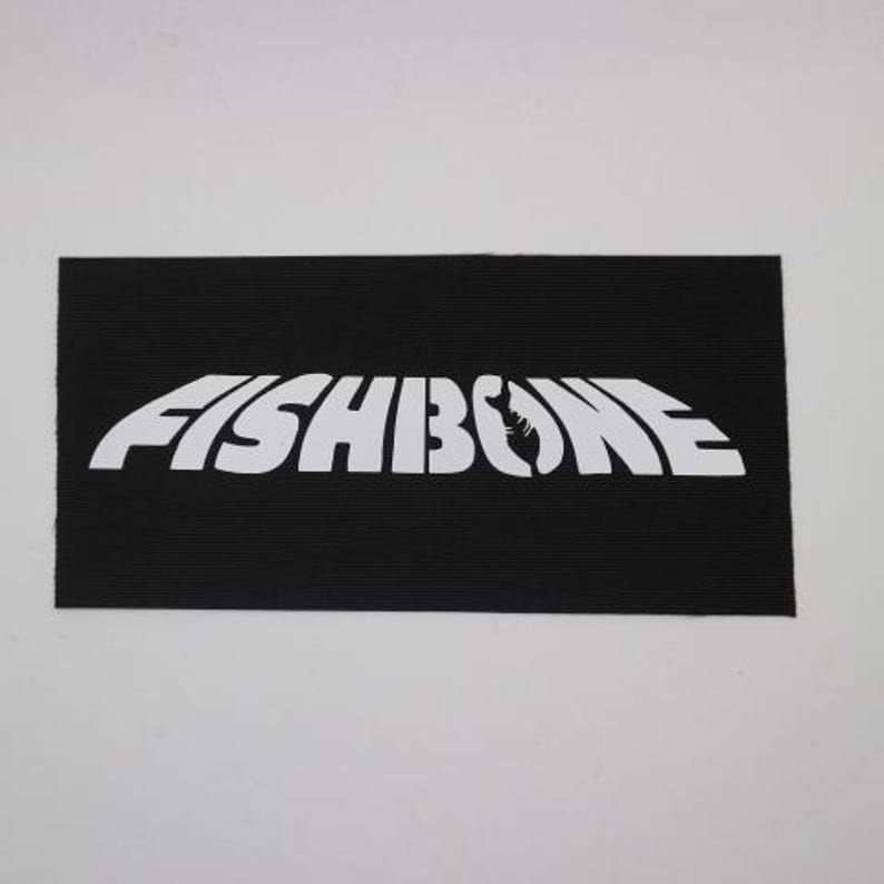 K&ouml;nnte beinhalten: Ein schwarzer rechteckiger Aufn&auml;her mit dem wei&szlig;en Text "FISHBONE". Das Wort "FISHBONE" ist in einer stilisierten Schriftart gehalten, wobei eine Fischskelettgrafik den Buchstaben "O" ersetzt. Der Aufn&auml;her hat eine gerippte Textur.