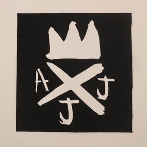 May include: Black fabric patch with a white crown, a white X, and the letters AJJ in white.