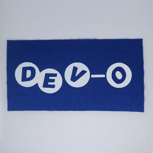 May include: A blue rectangular patch featuring the white text "DEVO-O". The letters are in a bold, rounded font. The patch has a textured appearance, and the background is a solid white.