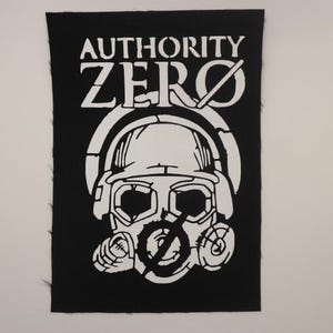 May include: Black and white embroidered patch with the text "AUTHORITY ZERO" and a graphic of a person wearing a gas mask.