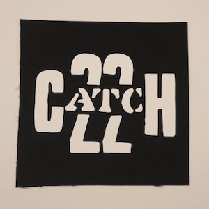 May include: A black square patch with the white text "CATCH 22". The text is in a bold, stylized font. The patch has a textured surface and a white border.