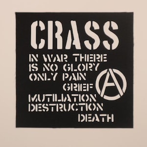 May include: Black square patch with white stenciled text reading "CRASS" and a statement about war. Anarchy symbol is on the right. The patch is on a light beige background.