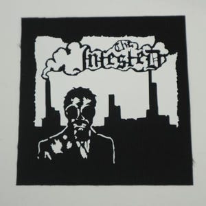 Peut inclure: &Eacute;cusson noir et blanc repr&eacute;sentant une silhouette en costume et lunettes, avec un paysage urbain et le mot "Infested" au-dessus. Le design est de style graphique audacieux.