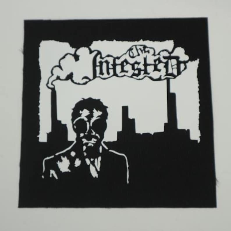 Peut inclure: &Eacute;cusson noir et blanc repr&eacute;sentant une silhouette en costume et lunettes, avec un paysage urbain et le mot "Infested" au-dessus. Le design est de style graphique audacieux.