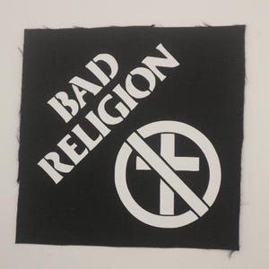 May include: A black square patch with the words "BAD RELIGION" in white, angled across the top left. A white circle with a cross through it is on the bottom right. The patch has a textured surface.