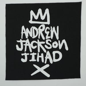 May include: A square, black patch with white text and a crown graphic. The text reads "ANDREW JACKSON JIHAD" with an "X" below. The design is a bold, graphic style.